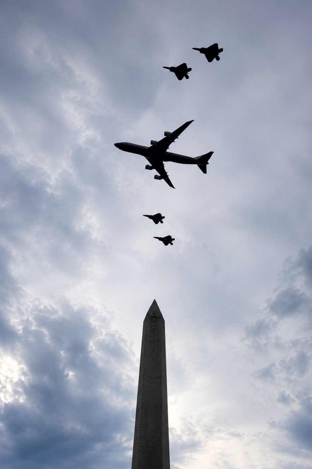 Air Force One and four fighter escorts fly above the Washington Monument under a cloudy sky